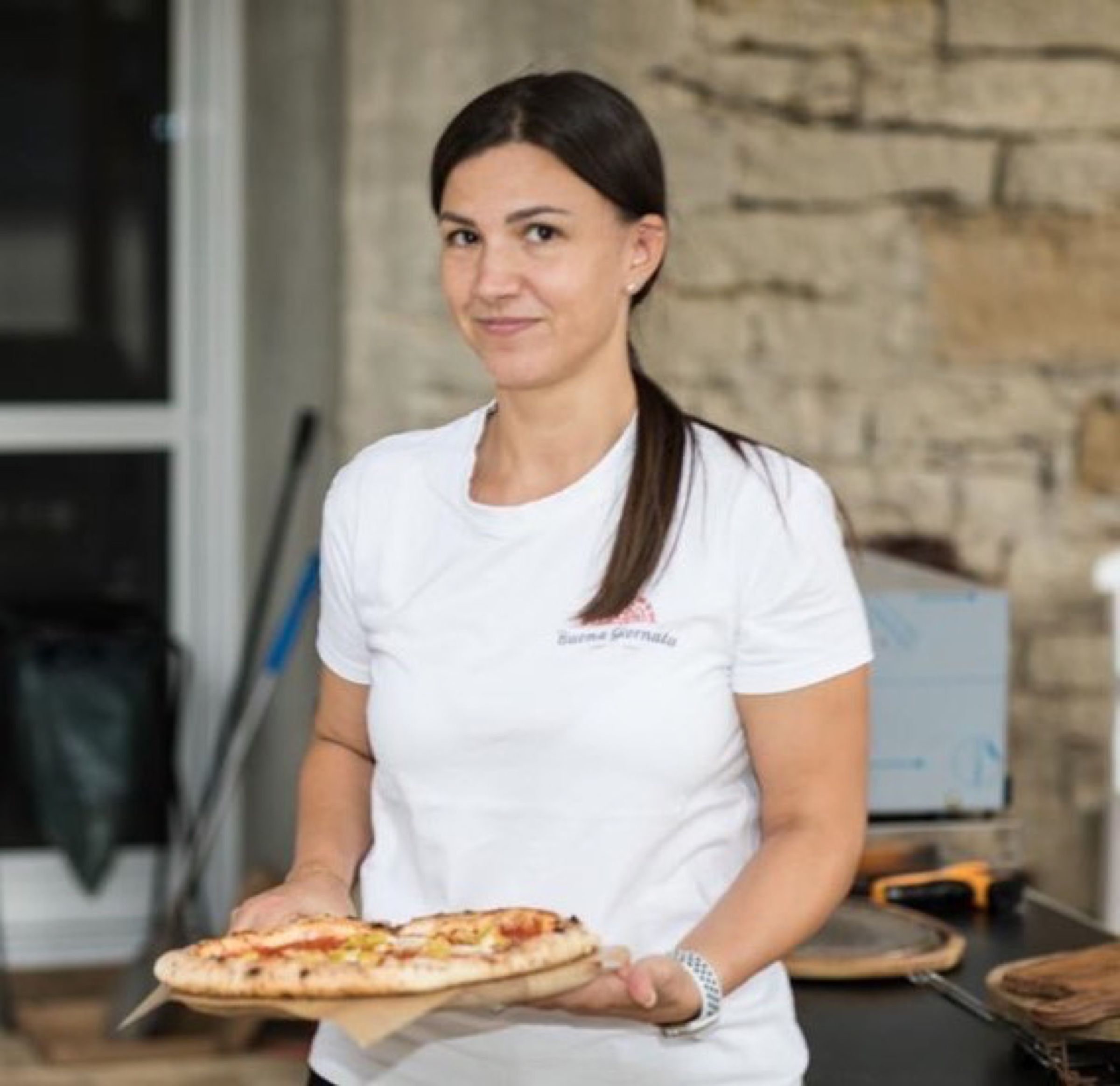 Frau im Buona-Giornata-T-Shirt mit einer Pizza auf einem Holzbrett