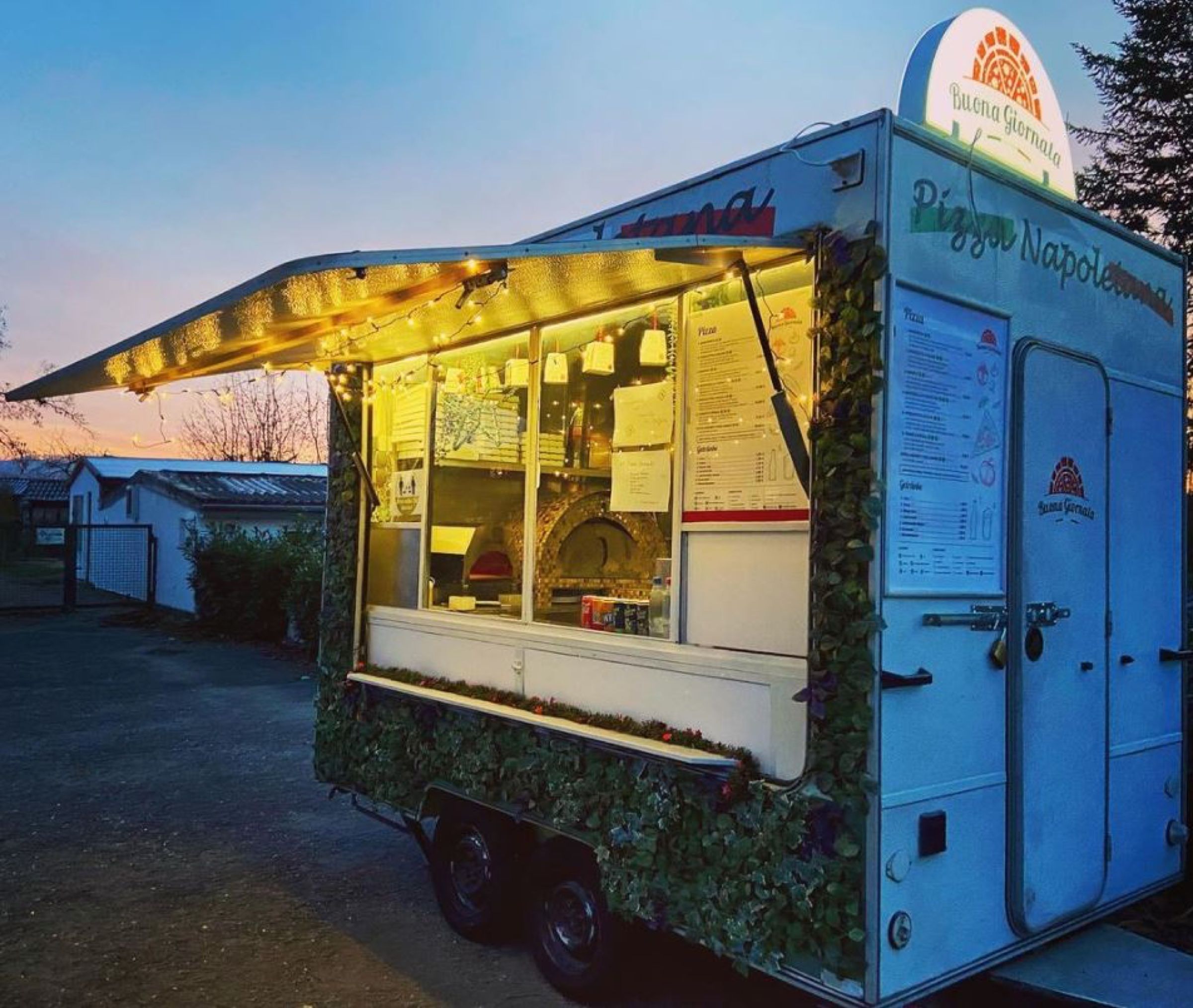 Beleuchteter Pizza Truck mit Buona-Giornata-Schild in der Abenddämmerung